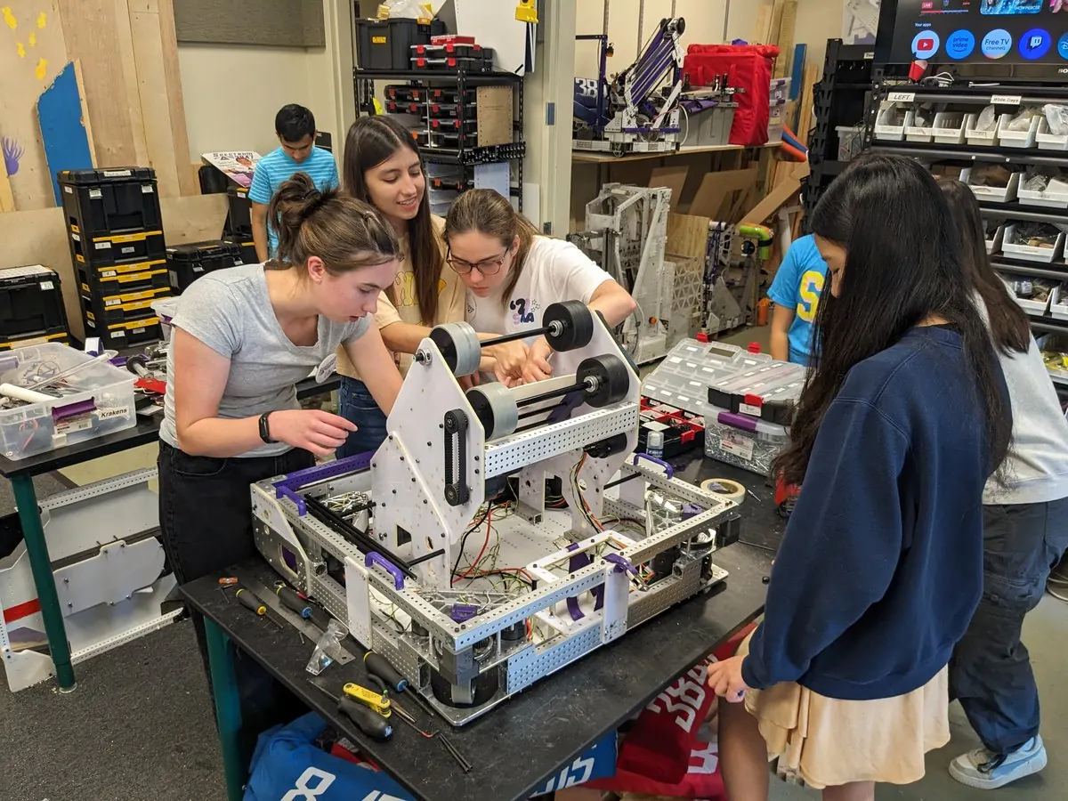 Three students assembling a robot mechanism on a workbench in the Spectrum lab